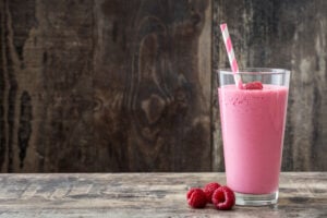 Raspberry smoothie in glass on wooden table.