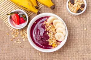 Açaí bowl topped with banana slices and granola, surrounded by fresh strawberries, bananas, and oats—ideal for a blog on top açaí bowl franchise opportunities in 2026.
